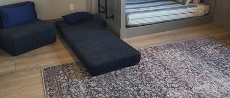 A compact room with a bunk bed, a small sofa, a bench, and a patterned rug.