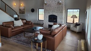 Amplia sala de estar con chimenea de piedra, sofás de cuero, una mesa de centro y una escalera.