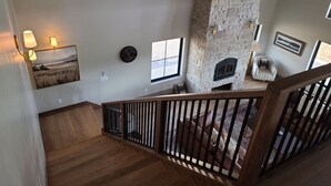 Una habitación amplia con chimenea de piedra, piso de madera y vista al exterior a través de un ventanal.