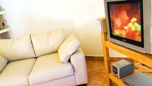 Un soggiorno con un divano color beige, una televisione su un mobile in legno e un tavolino con dispositivi elettronici.