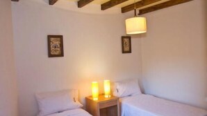 Una stanza piccola e accogliente con due letti singoli, un comodino in legno con una lampada e un soffitto a vista con travi.
