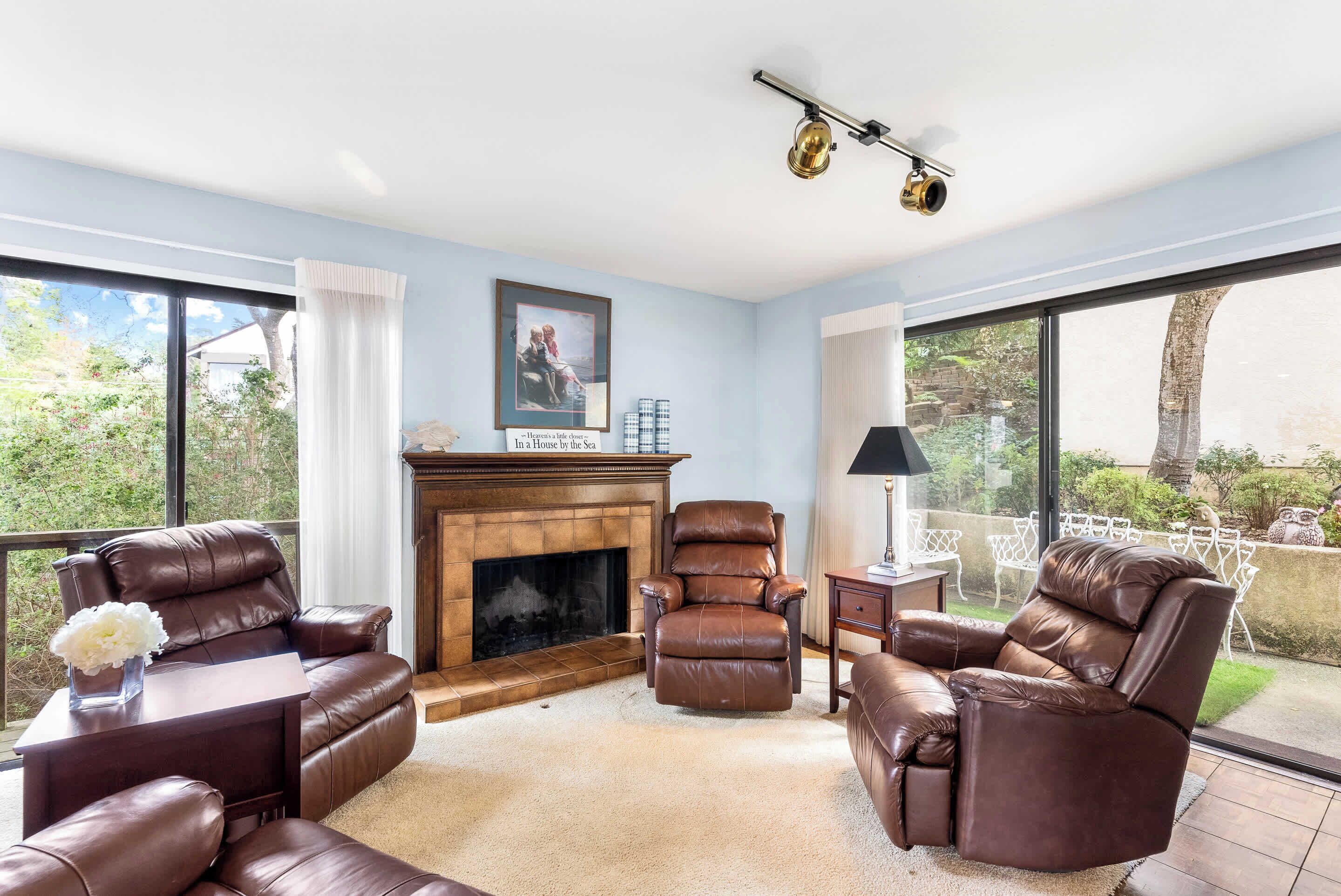 A living room with leather sofas, a fireplace, and large windows offering a view of the outdoors.