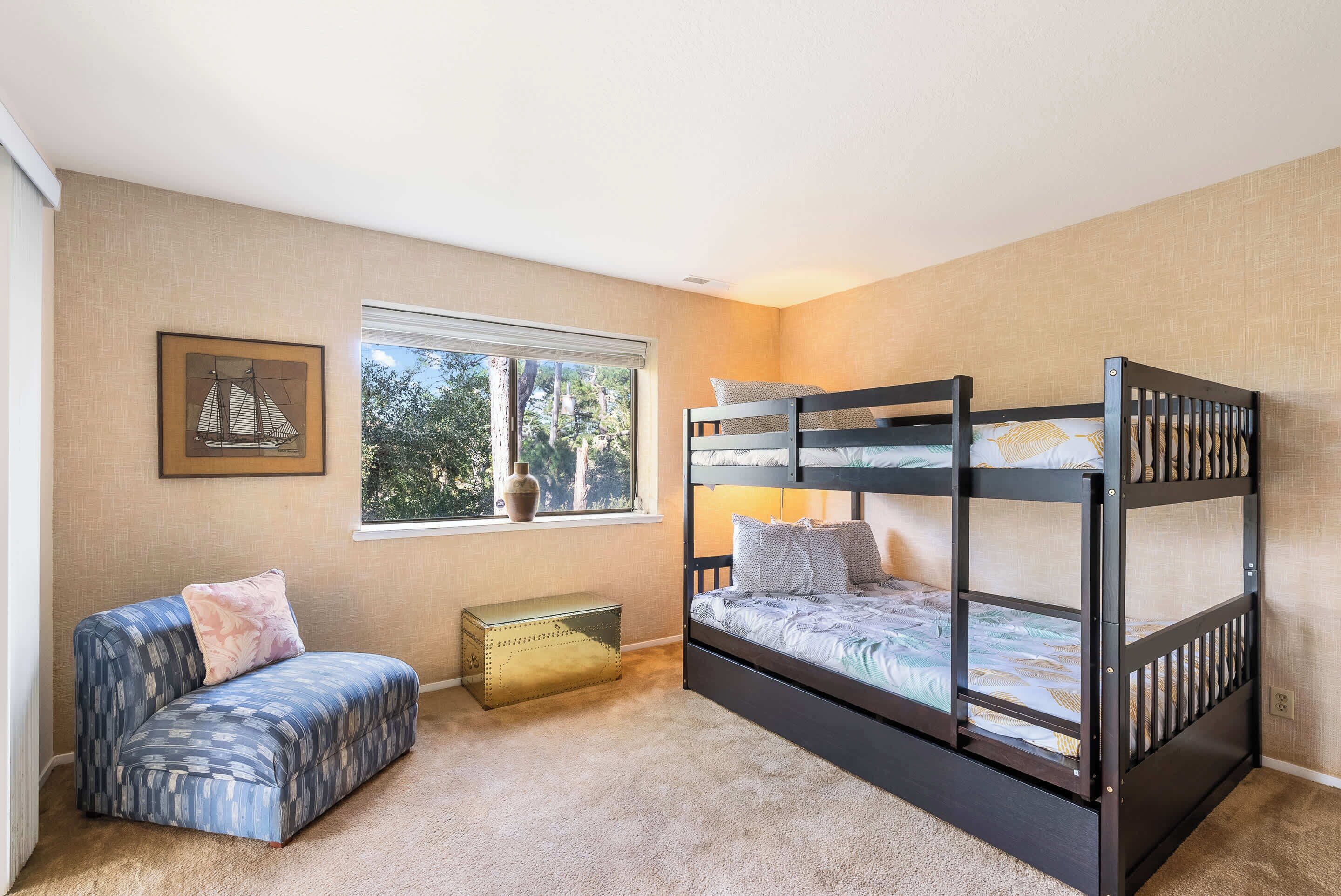 Una habitación con una cama individual alta, un sofá, una ventana y un florero en el alféizar.