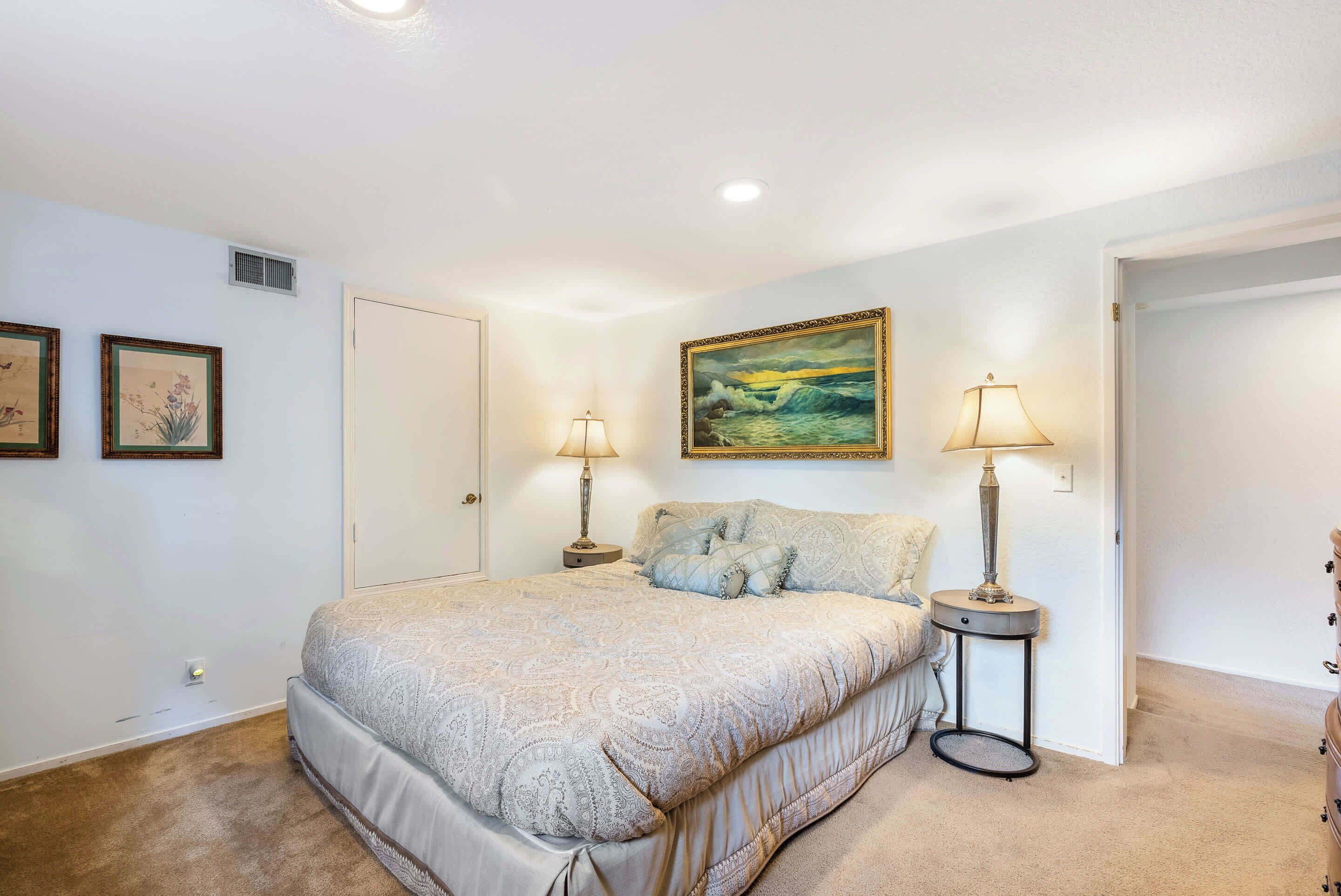 A bedroom with a large bed, two bedside lamps, a painting on the wall, and a door to another room.
