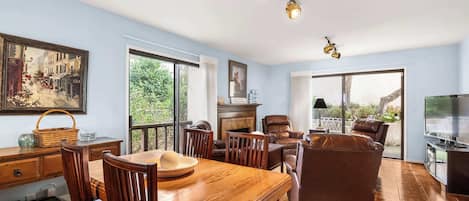 Ein geräumiges Wohnzimmer mit einem Holzesstisch, Ledersesseln, einem Kamin und einem großen Fenster mit Blick ins Freie.