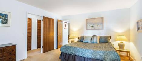 A bedroom with a large bed, a dresser, a nightstand, and a door leading to another room.