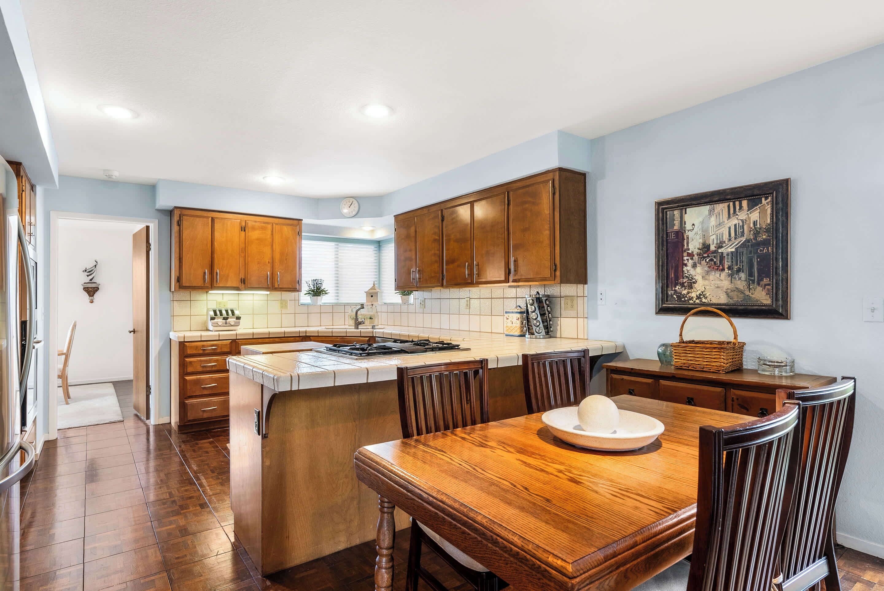 Una cocina con armarios de madera, una isla central y un comedor con mesa y sillas de madera.