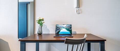 A modern room with a wooden desk, a laptop, a vase with flowers, and a wall-mounted telephone.