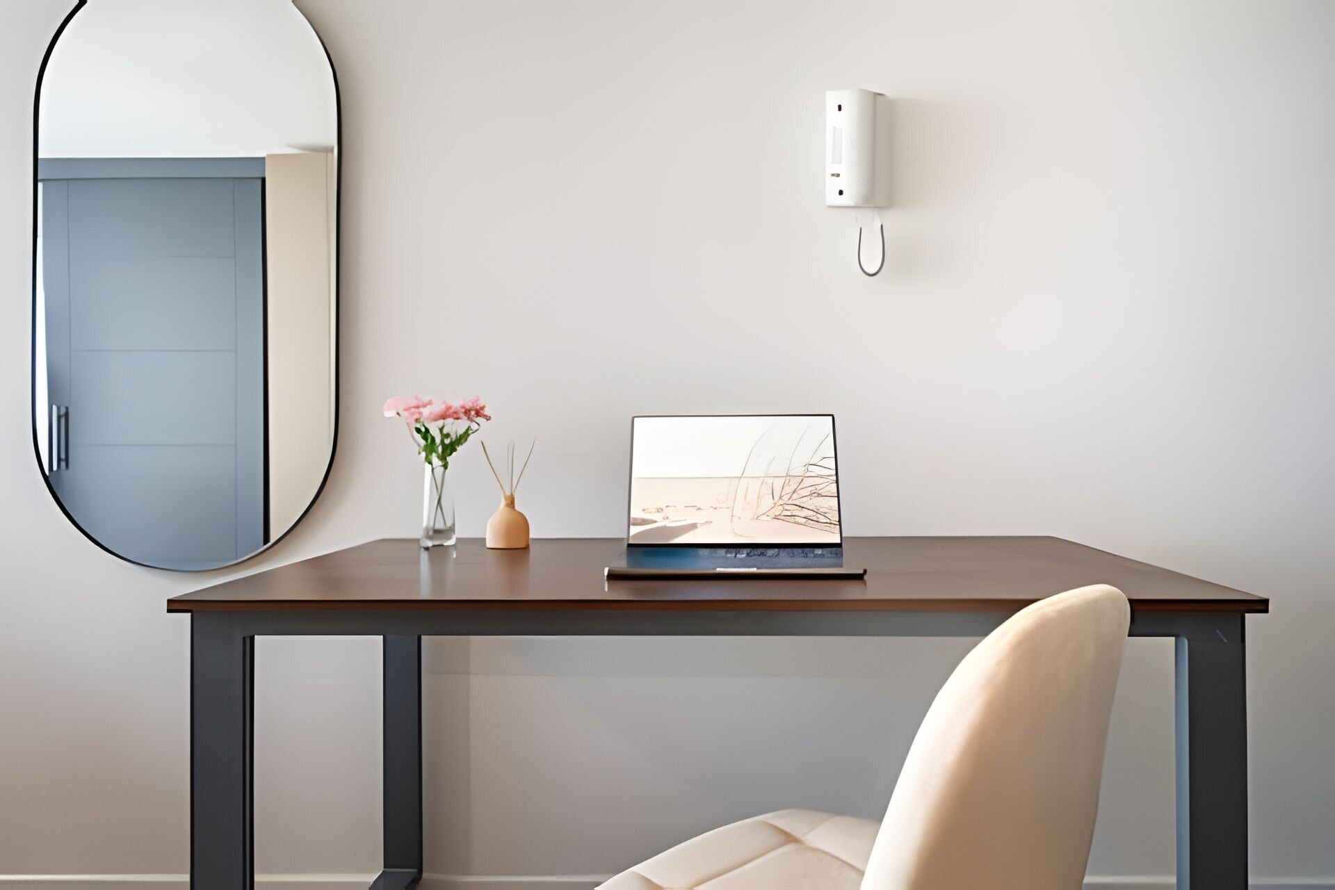 Een moderne kamer met een ronde spiegel, een laptop op een houten tafel, een vaas met bloemen en een wandlamp.