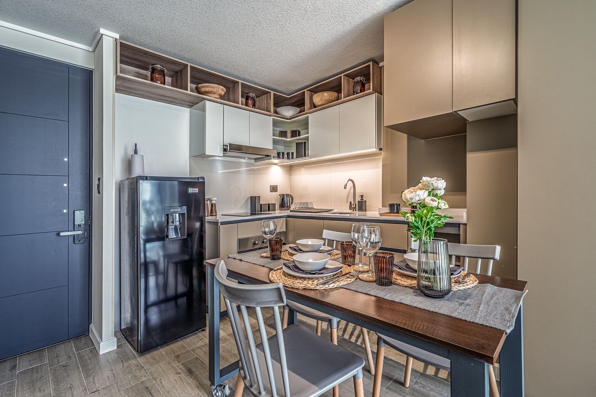 Una cocina moderna con refrigerador empotrado, armarios de madera y un comedor con una mesa para dos.