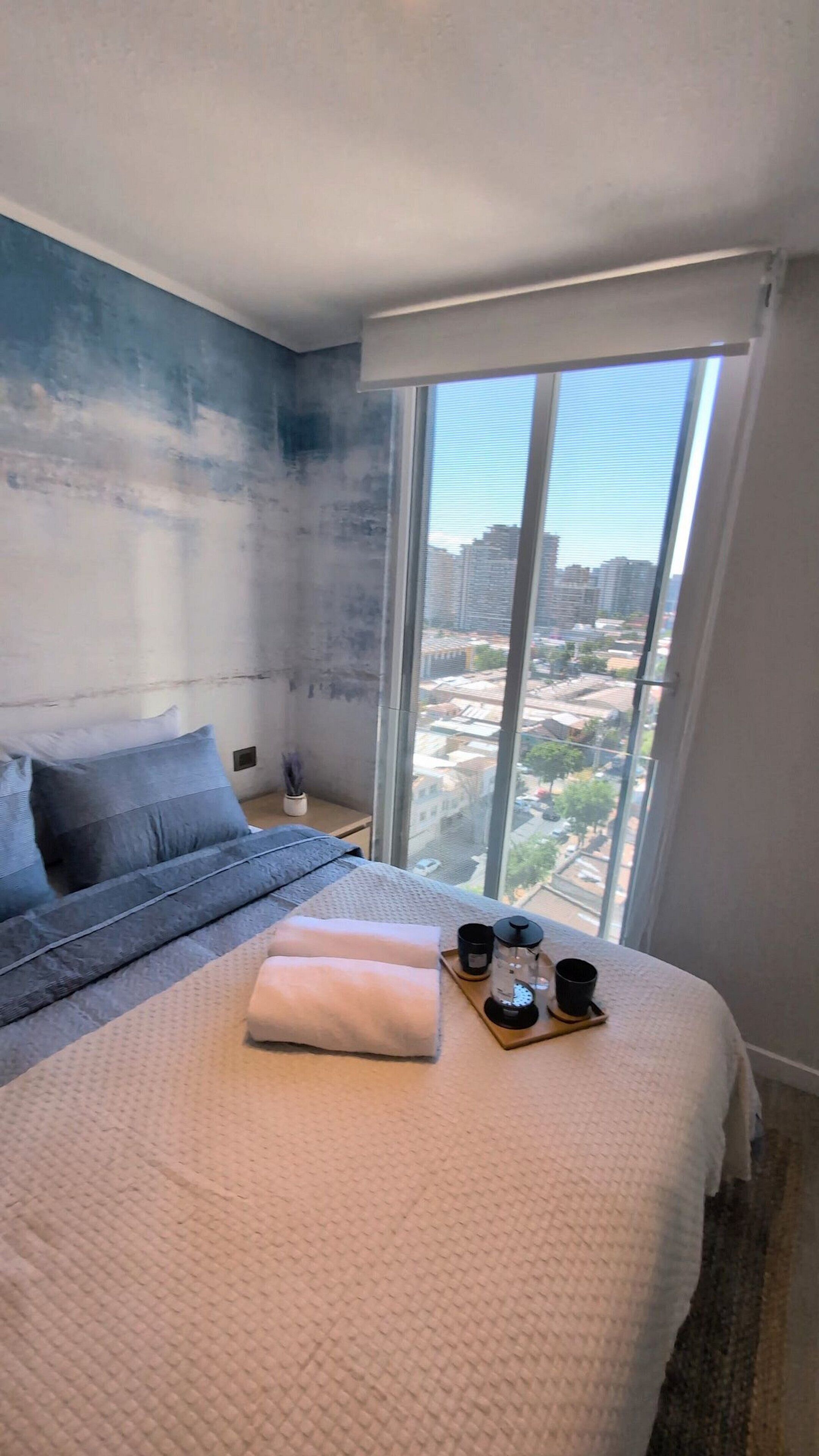 A bedroom with a large bed, a view of the city through a window, and a cityscape visible outside.