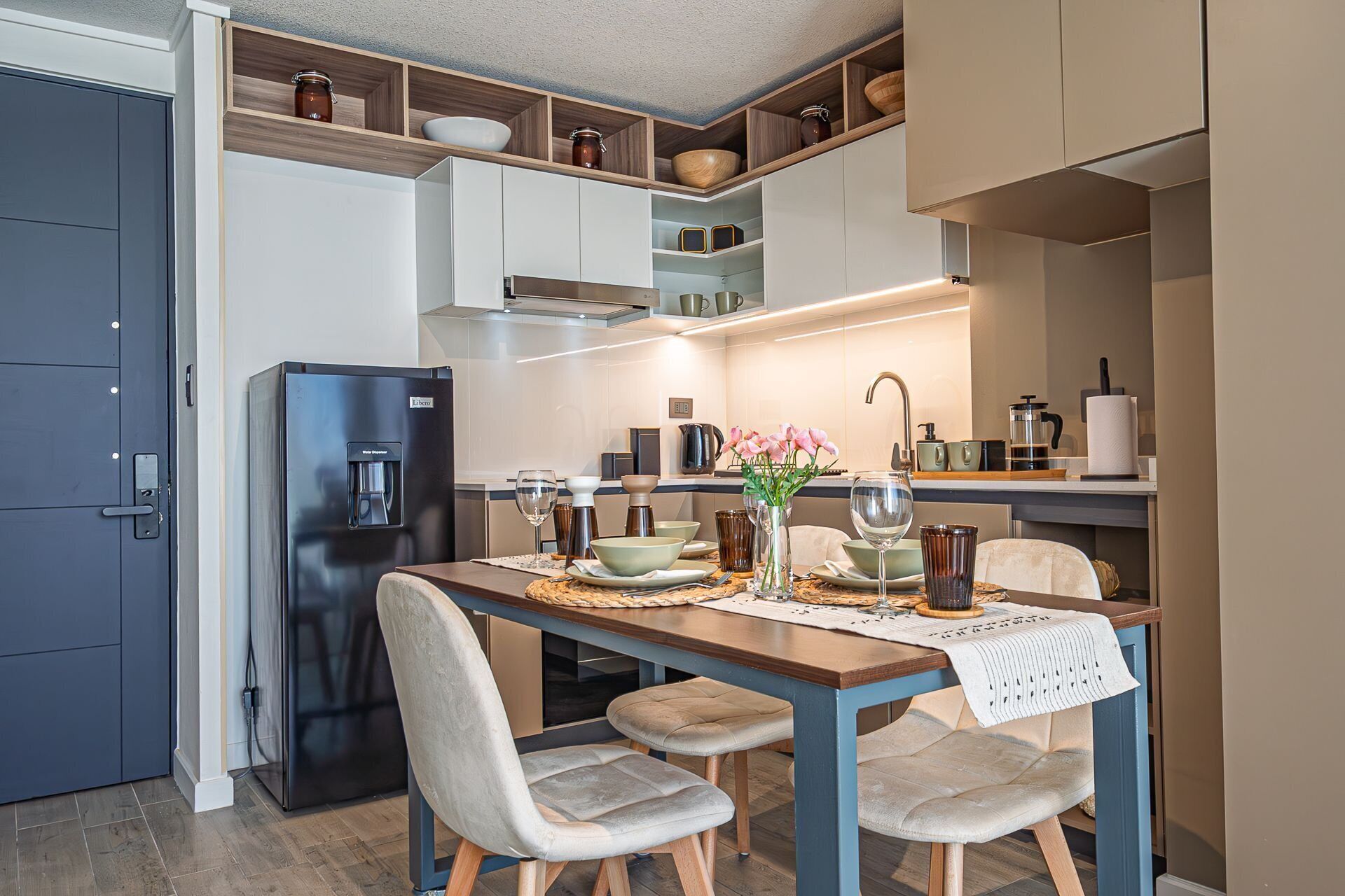 A modern kitchen with a built-in water dispenser, a dining table with chairs, and a variety of kitchenware and decorative items.