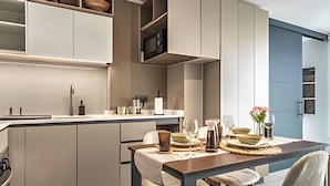 A modern kitchen with integrated appliances, a dining area with a wooden table and chairs, and a blue accent wall. - Santa Elvira Apartments (Santiago)