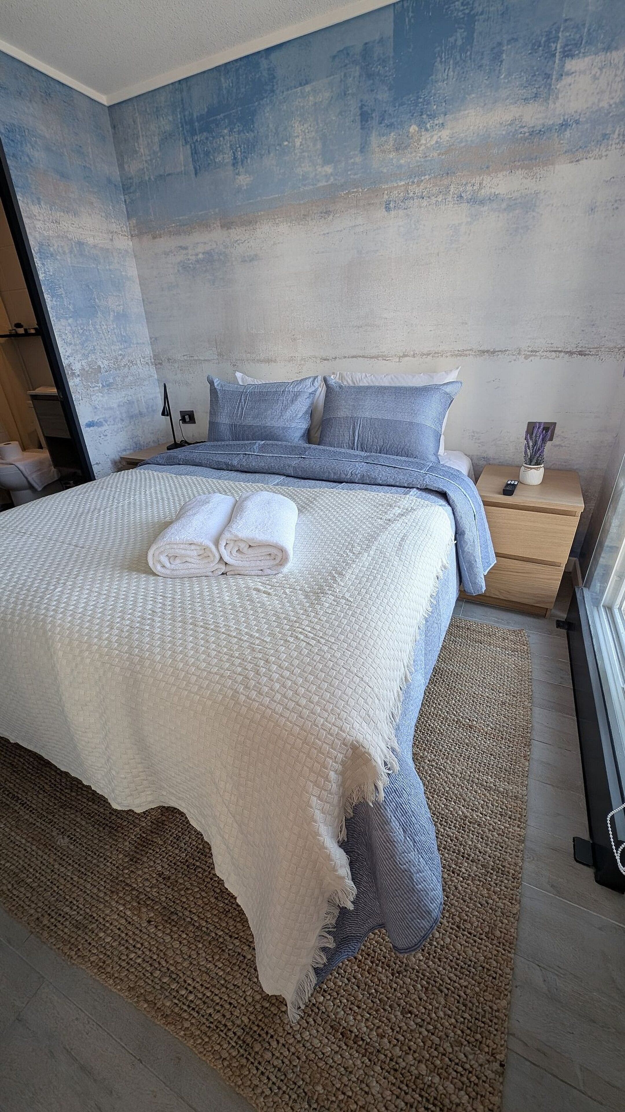 Un dormitorio con una cama grande, una mesita de noche, un estante en la pared y una ventana.