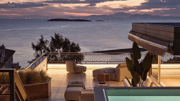 A rooftop terrace with a pool, seating area, and a view of the sea at dusk.