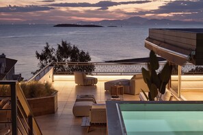 A rooftop terrace with a pool, seating area, and a view of the sea at dusk.