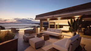 A modern outdoor living area with a sofa, ottoman, and coffee table, overlooking a body of water.