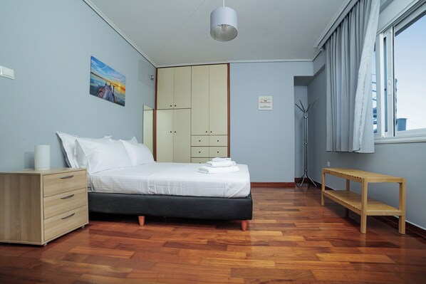A bedroom with a bed, wooden drawers, a bench, a wardrobe, and a painting on the wall.