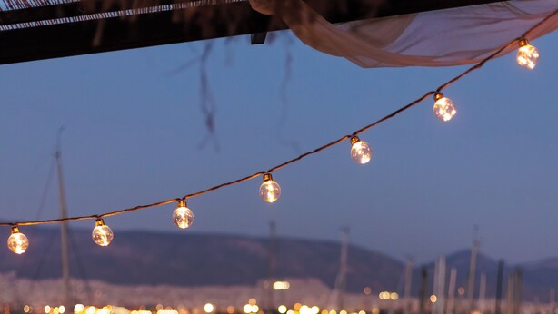 A balcony with a view of a marina at dusk, featuring string lights and a bench. - Seaside Grey Pearl Villa 
Sea Views, Ideal for Artists & Dreamers (Pireas)