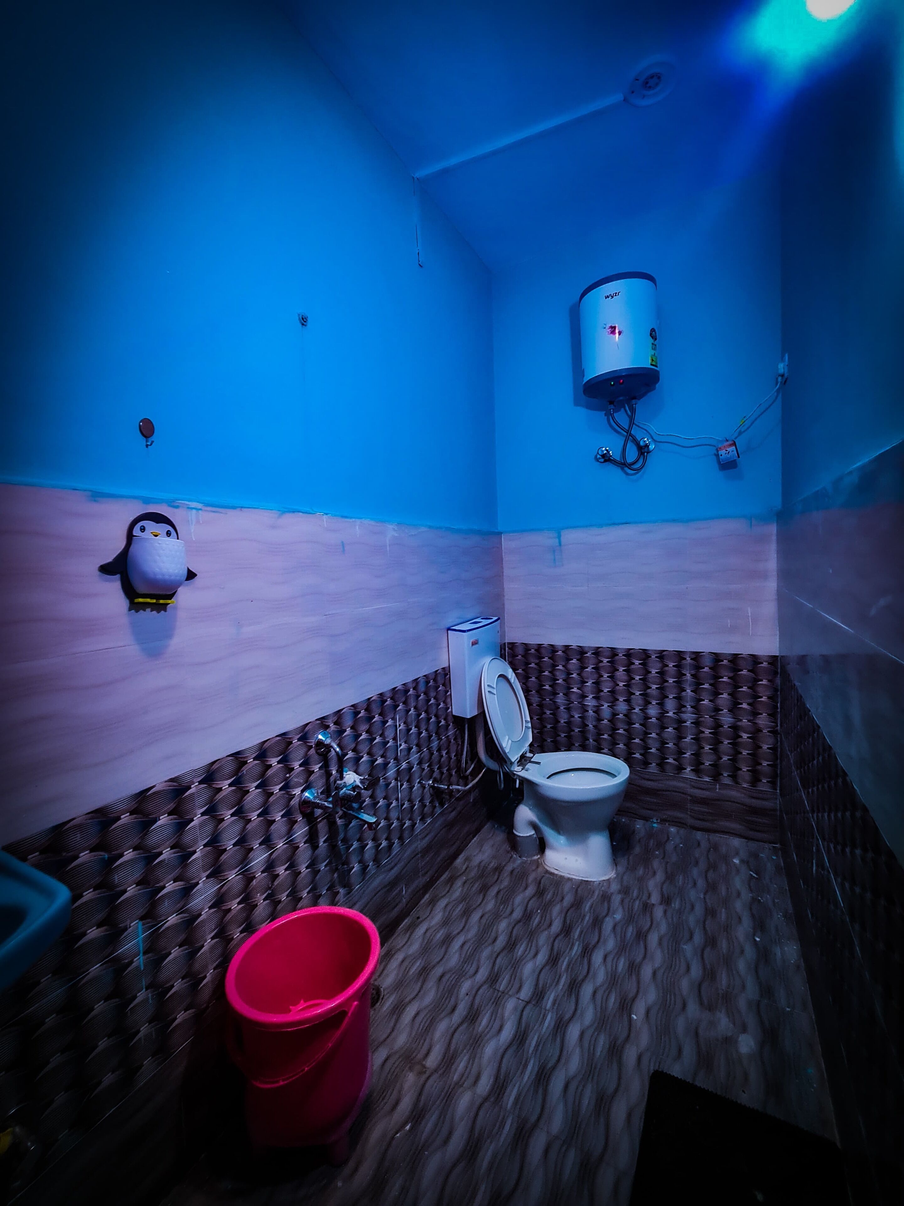 A small, compact bathroom with a toilet, a red bucket, and a wall-mounted water heater.