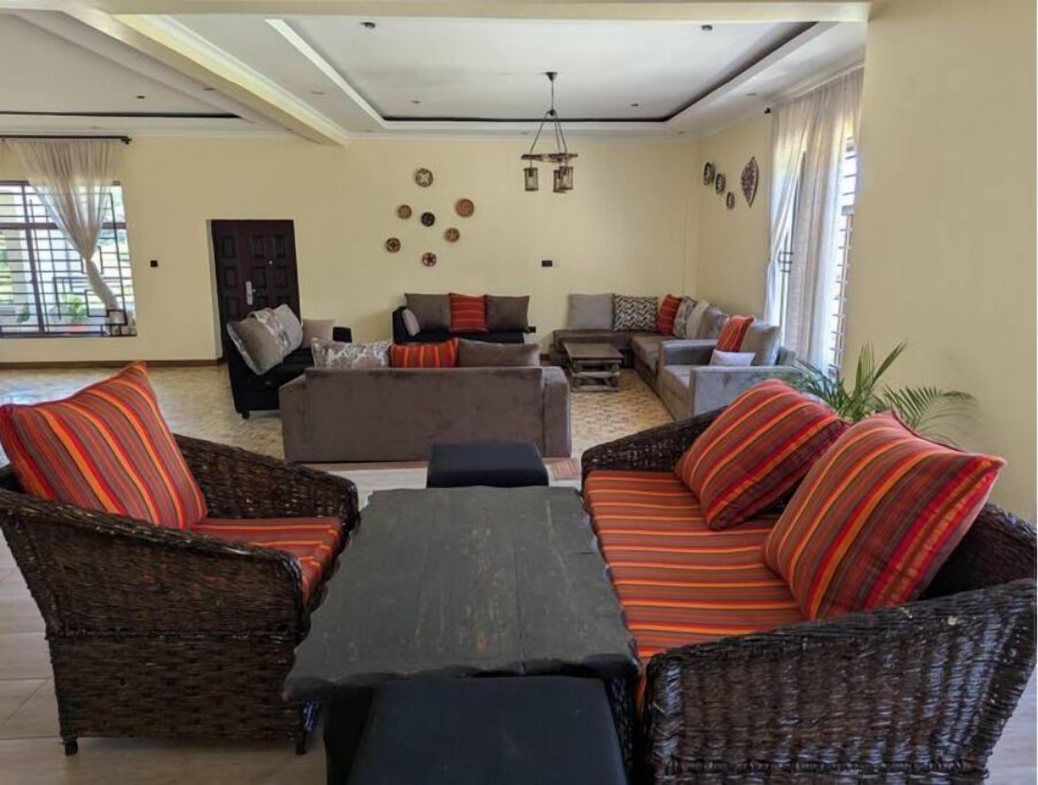 A living room with a sofa set, a coffee table, and a wicker chair. There is a door and a window with curtains.