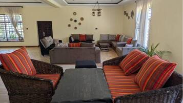 A living room with a sofa set, a coffee table, and a wicker chair. There is a door and a window with curtains.