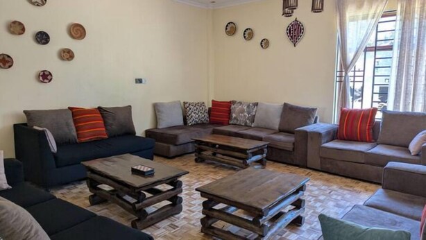 A living room with a sofa set, a coffee table, and decorative wall art. - Luxury Kingsuite Room with Balcony in Karen Nairobi + Halfboard (Nairobi)