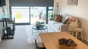 A modern living room with a sofa, a dining table, and a large window with a view of the outdoors. - Scandi City Escape | Walk Everywhere, Near Stadium (Christchurch)