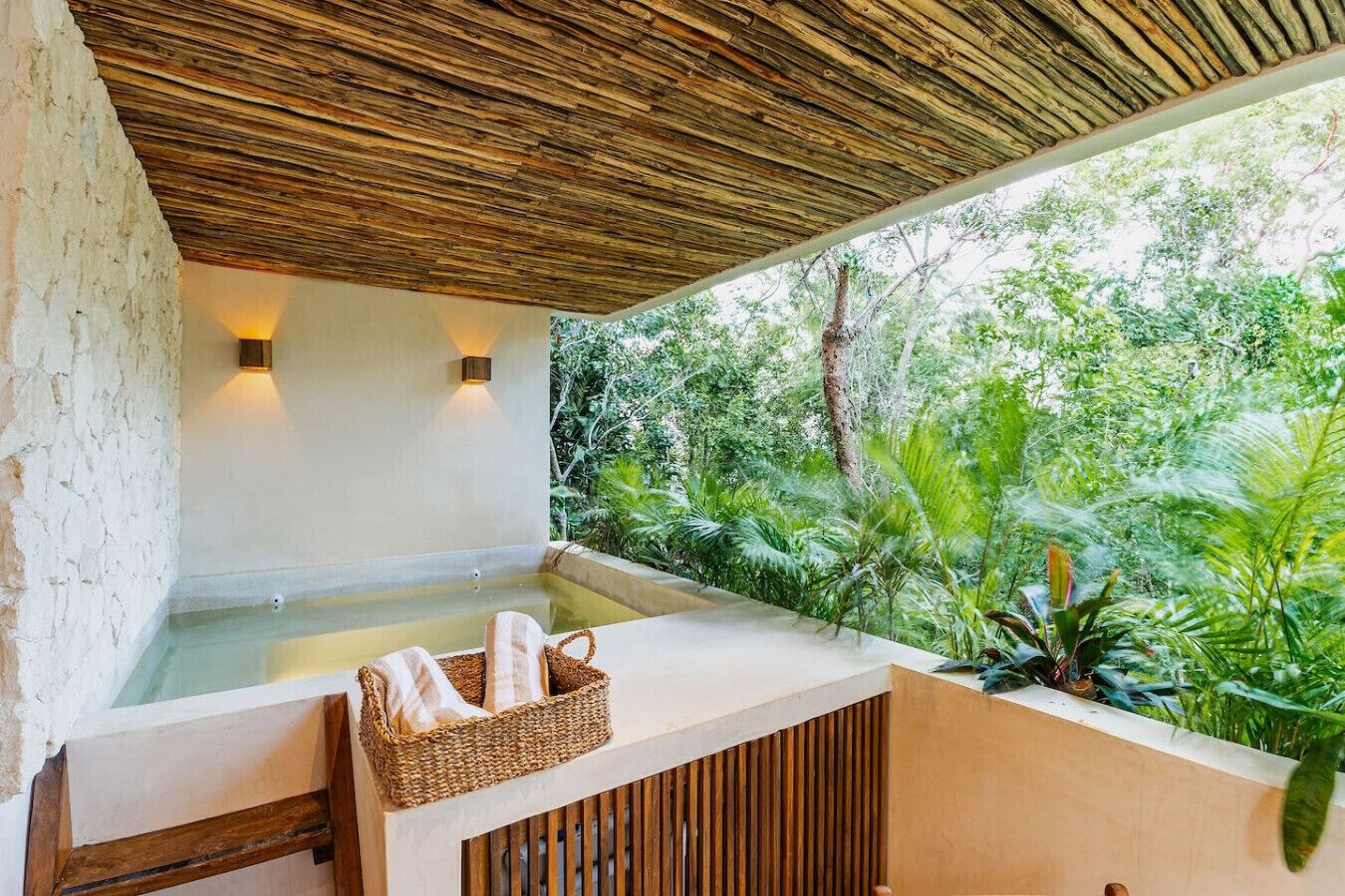 A spa area with a wooden ceiling, a hot tub, and a view of lush greenery.