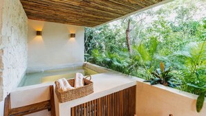 A spa area with a wooden ceiling, a hot tub, and a view of lush greenery.