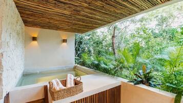 A spa area with a wooden ceiling, a hot tub, and a view of lush greenery.