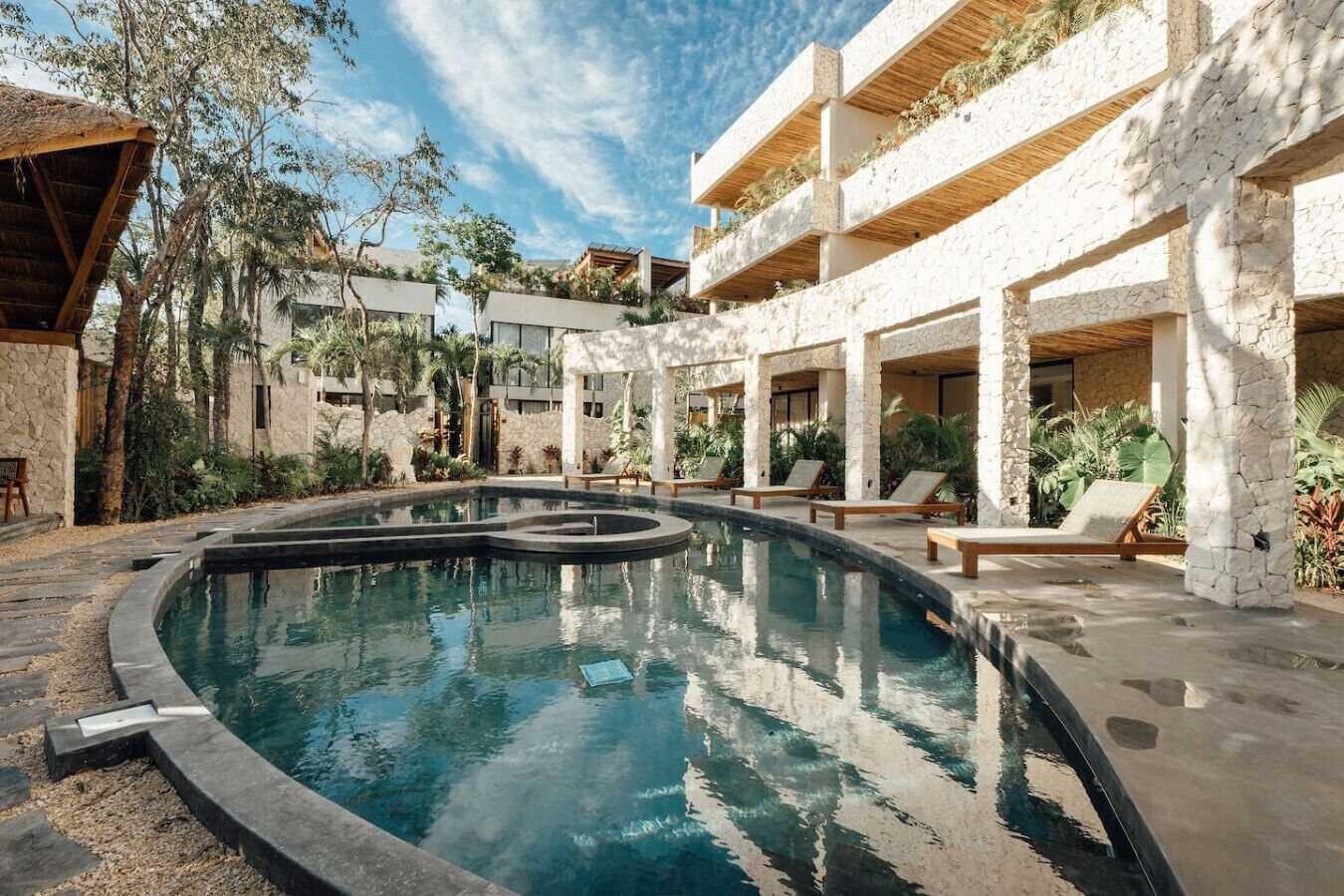 A swimming pool with lounge chairs and a stone building with a thatched roof.