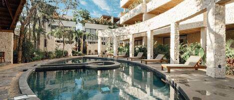 A swimming pool with lounge chairs and a stone building with a thatched roof.