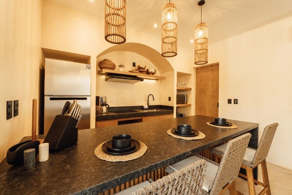 Een moderne keuken met een centraal eiland, ingebouwde apparatuur en een eethoek met rieten stoelen.