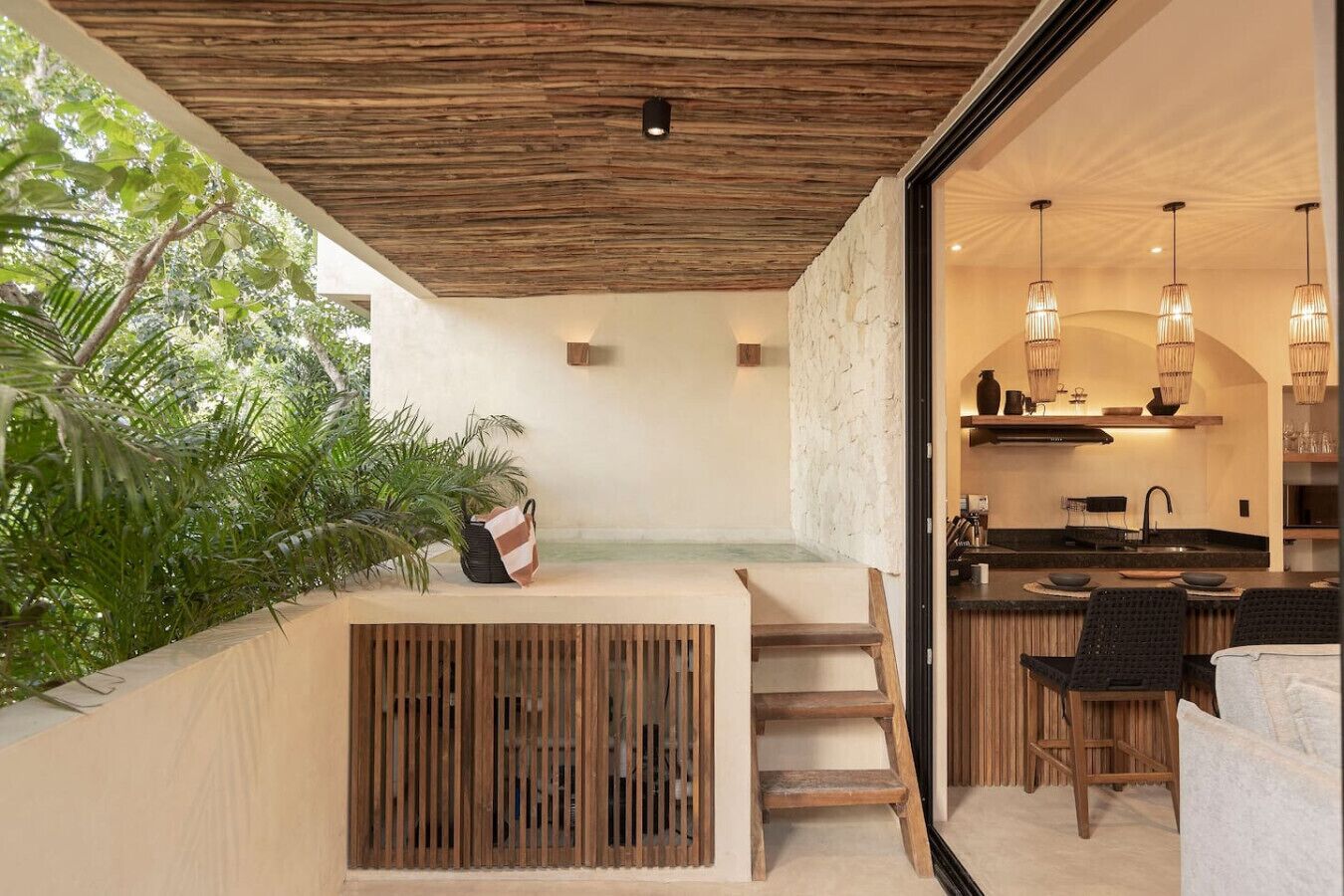 A modern kitchen with a stone wall, wooden ceiling, and a dining area with a bench and chairs.