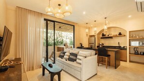 A modern living room with a sofa, a coffee table, and a dining area with a kitchen in the background. - Jungle Cove w private pool n concierge. 3p.  2 TVs (Tulum)