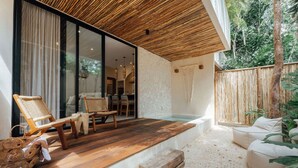 A modern outdoor patio with wooden flooring, a hot tub, wicker furniture, and a view of the interior through large glass doors. - 1BR Hidden Gem–Priv Pool+Garden at Launch Price (Tulum)