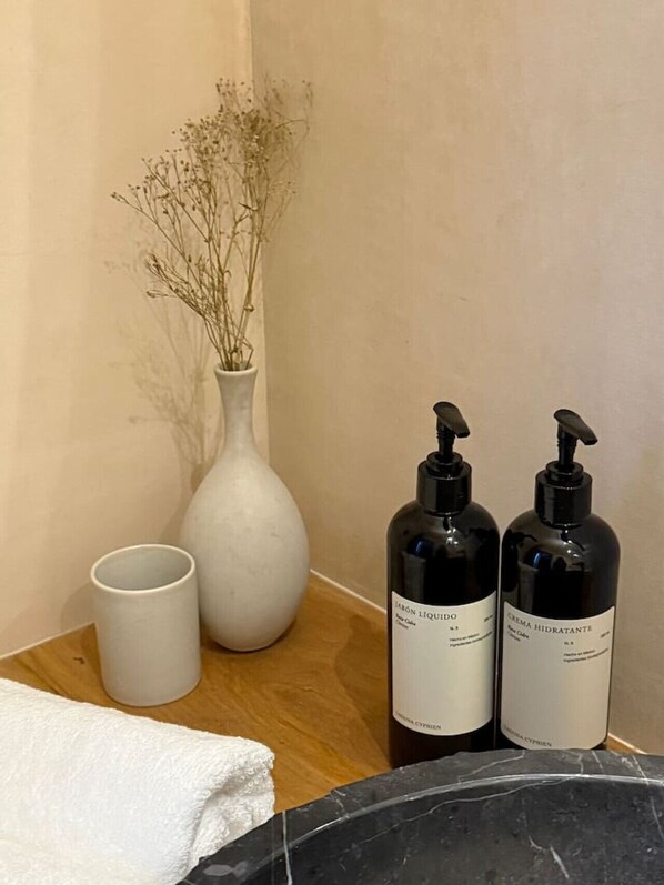 A bathroom vanity with a white vase, a white cup, and two black bottles of lotion.