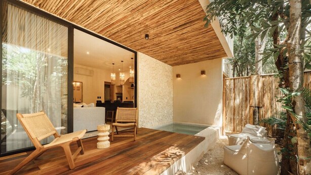 A modern outdoor living area with a wooden deck, a seating area with a chair and a small table, and a hot tub. - Jungle Luxury: 1-BR, Plunge Pool, Fully Equipped (Tulum)