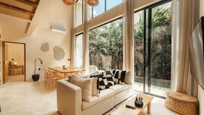 A spacious living room with a large window, a sofa, a coffee table, and a dining area. - Luxe Villa, 12p, 2 private pools, grill w/concierge (Tulum)