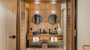 A modern bathroom with wooden slats, two round mirrors, a wooden vanity with two sinks, and a glass shower enclosure. - Luxe Villa, 12p, 2 private pools, grill w/concierge (Tulum)