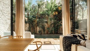 A room with a wooden table and chairs, a sofa with a throw blanket, and a view of a lush garden through large windows. - Luxe Villa, 12p, 2 private pools, grill w/concierge (Tulum)
