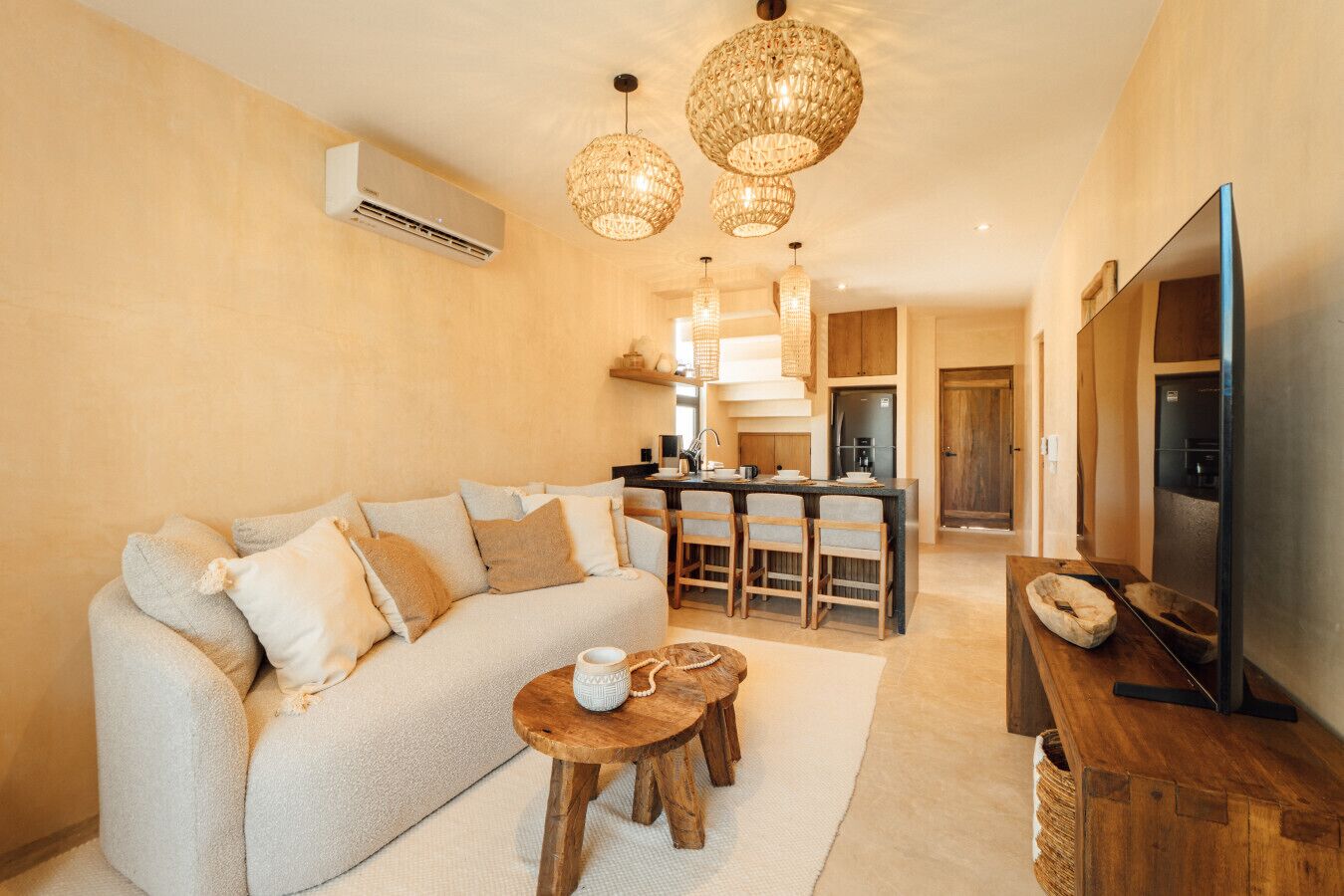 A cozy living room with a sofa, a coffee table, and a TV. There is a kitchen area with a bar and a refrigerator.