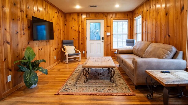 Una sala de estar acogedora con paredes de madera, un televisor de pantalla plana, un sofá, un sillón, una mesa de centro y una planta grande.