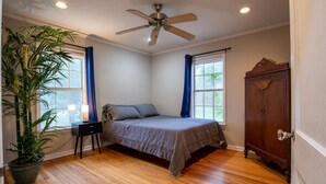 Un dormitorio con cama, ventilador de techo, armario de madera y planta en maceta.