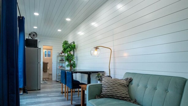 A cozy living area with a sofa, a dining table, chairs, and a kitchen in the background. - Container-Home 15 mins from FWTX | Pets Welcome (Fort Worth)