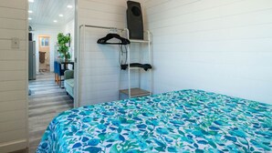 A room with a bunk bed, a hanging chair, a speaker, and a door leading to a kitchenette. - Container-Home 15 mins from FWTX | Pets Welcome (Fort Worth)