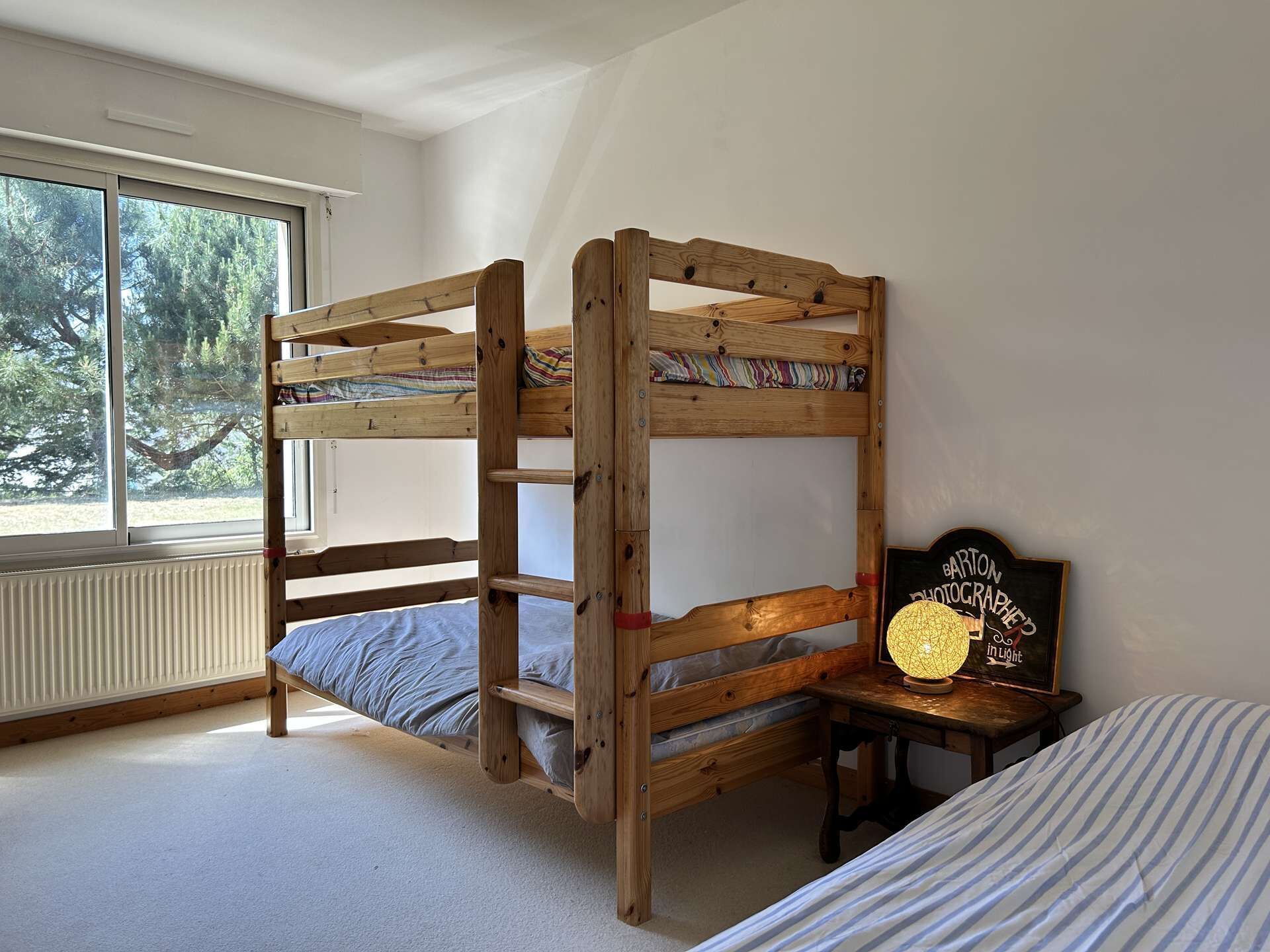 Ein Schlafraum mit Etagenbetten, einem Fenster, einem kleinen Tisch mit Lampe und einem gerahmten Schild.