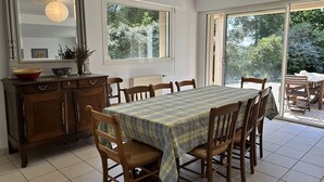 A dining area with a table set for six, flanked by wooden chairs, a wooden cabinet with a mirror, and a window with a view of greenery. - Large family house for 11 guests near the beach in Fréhel | Ref 113 (FREHEL)