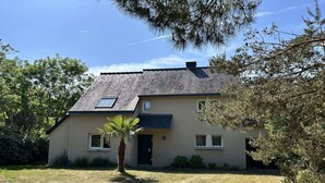 A two-story house with a sloped roof, a small front porch, and a palm tree in the yard. - Large family house for 11 guests near the beach in Fréhel | Ref 113 (FREHEL)